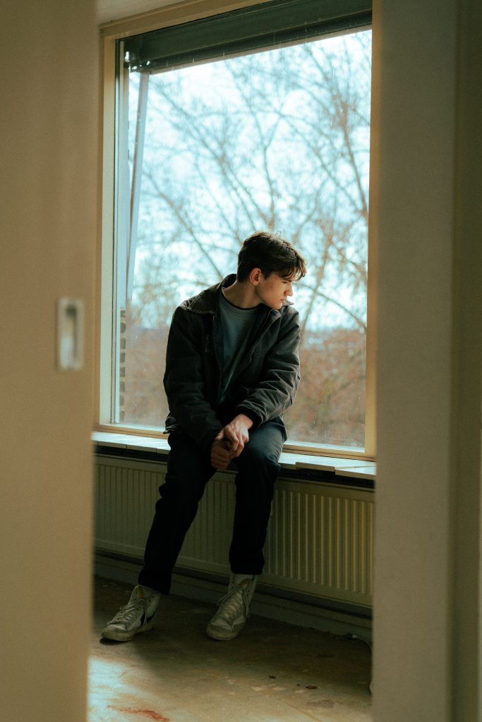 Adolescente sentado junto a una ventana en actitud reflexiva